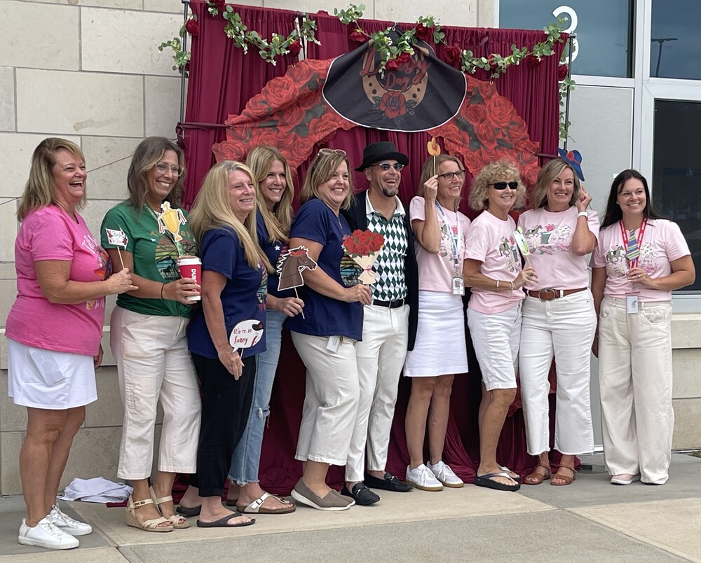 staff dressed up for day at the races pose in front of kentucky derby themed backdrop