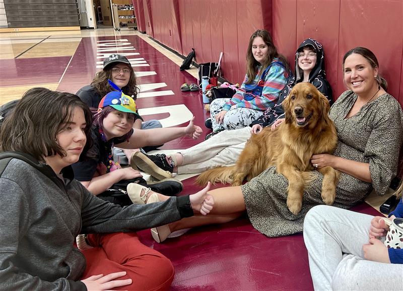 students sit on gym floor with assistant principal and maverick, the good citizen pup