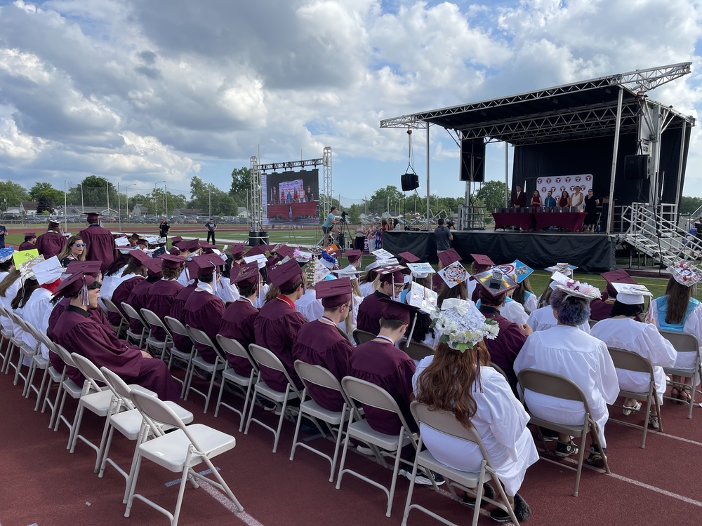 graduation photo from the back with grads in foreground and stage and admins in background