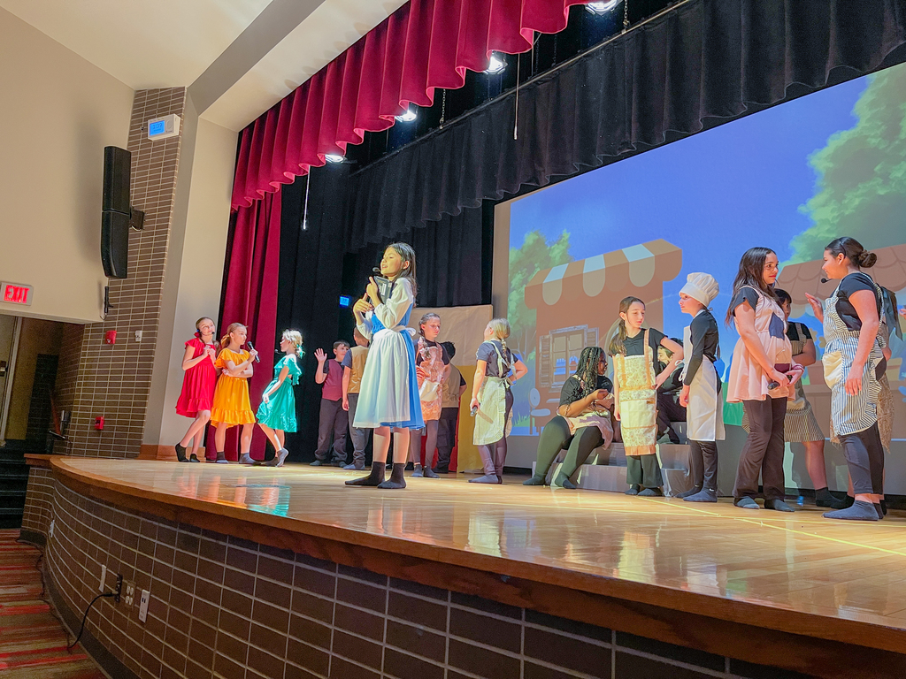 belle sings on stage with cast dancing around her