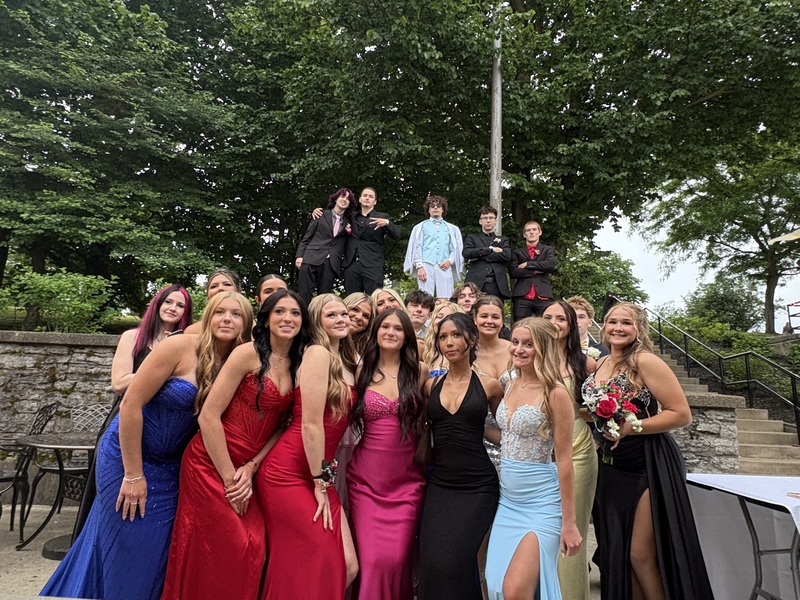 students pose in prom wear in front of trees
