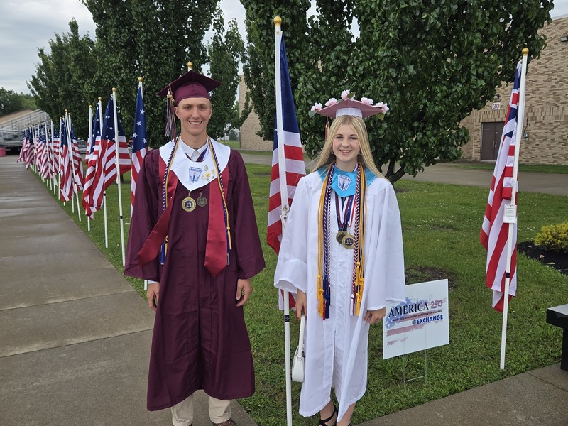 students pose by line of flags on walkway to stadium