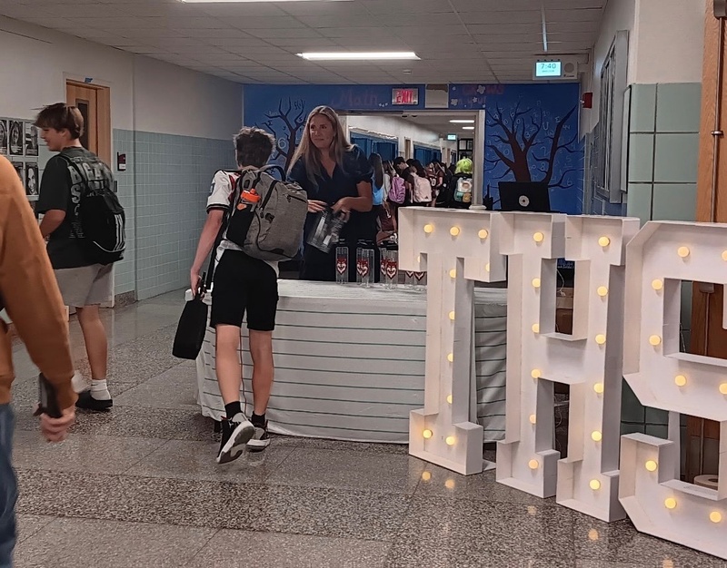 principal handing waterbottle to student with THS sign in foreground