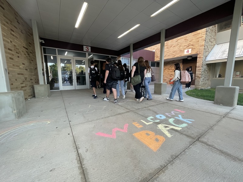 welcome back written in chalk on sidewalk as students walk into building