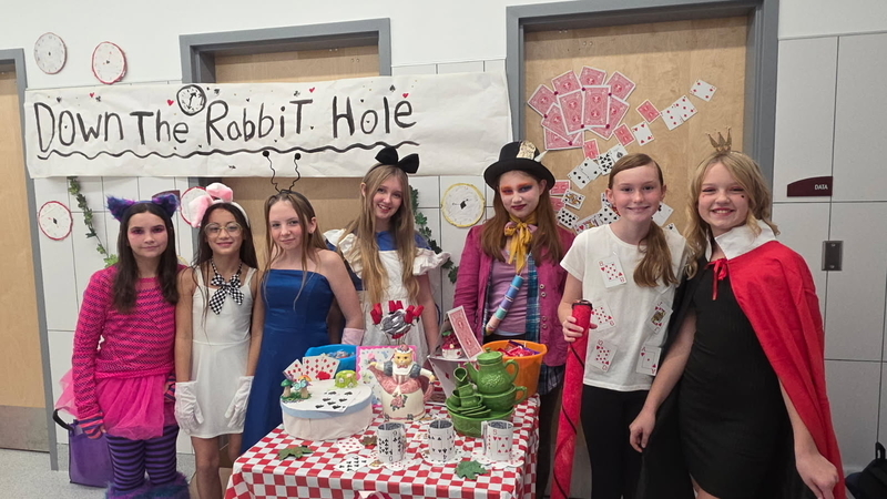 students pose at their alice in wonderland trunk or treat table