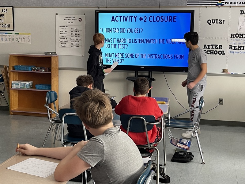 students stand at smart board explaining a lesson to classmates
