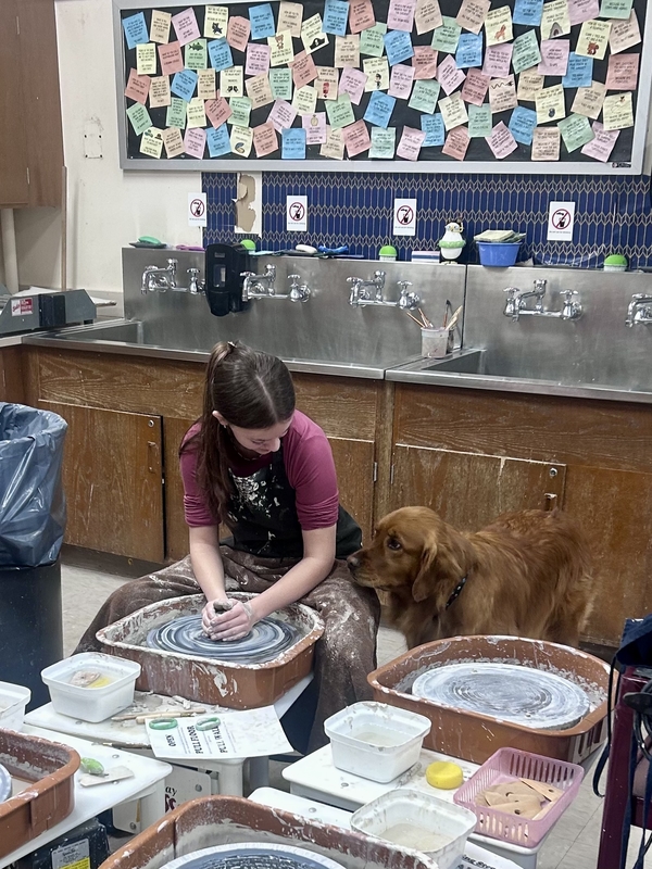 art student working on clay project , looking at dog who looks at the project