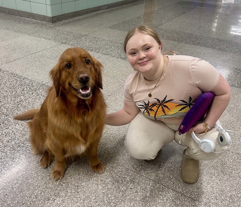student crouches down to pose with sitting dog in hallway