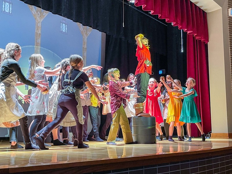 Gaston flexes on stage surrounded by cast members