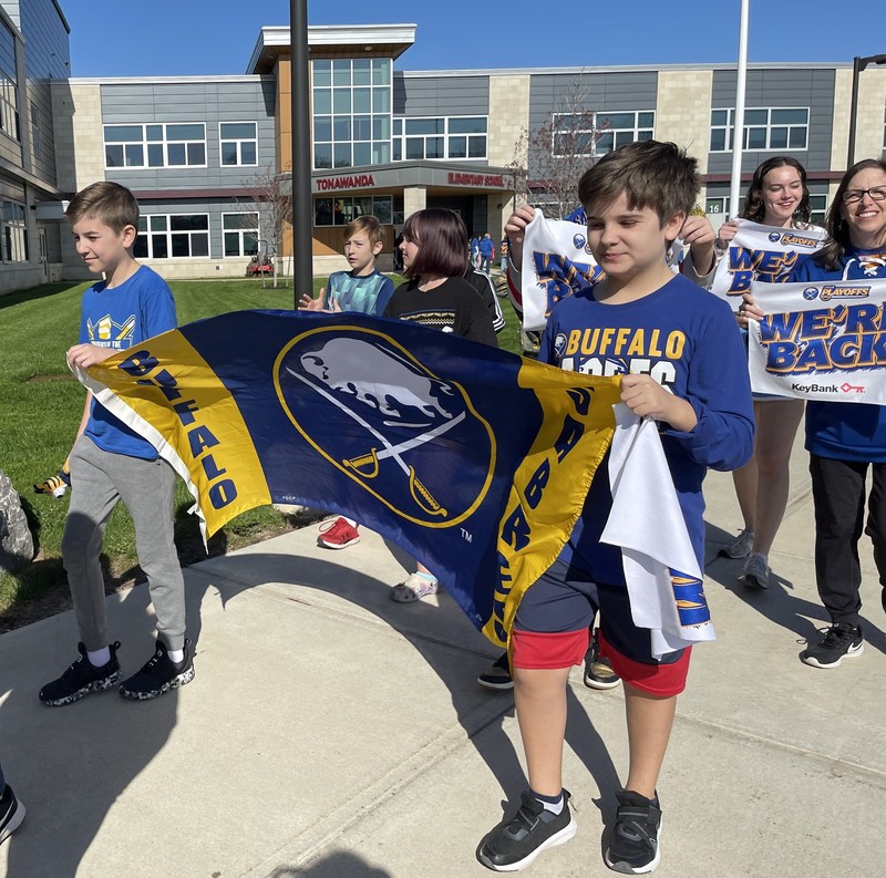 students carry sabres banner with teachers holding we're back flags behind