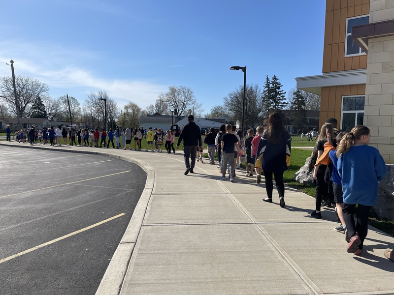 students walk in parade along sidewalk around school
