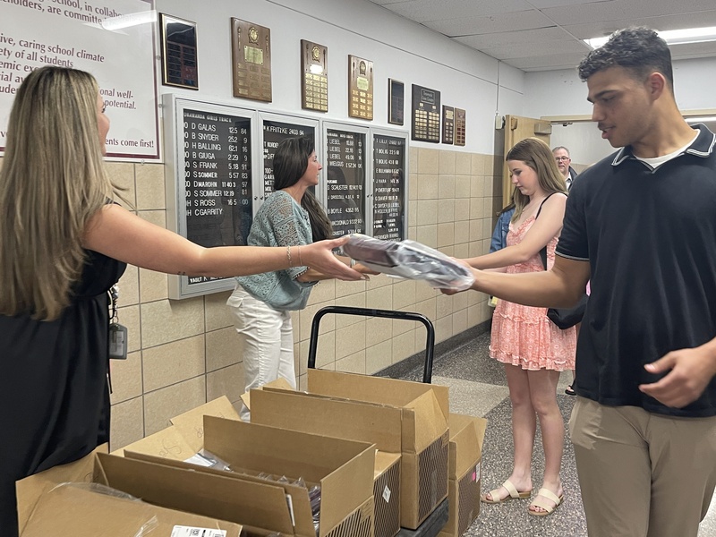 assistant princstaff hands out caps and gowns to students lined up