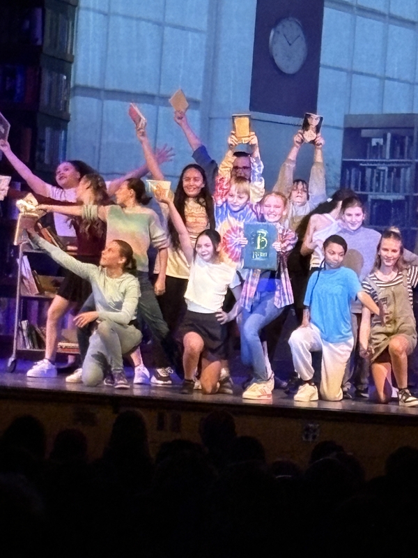 cast of between the lines performing on stage with hands in the air