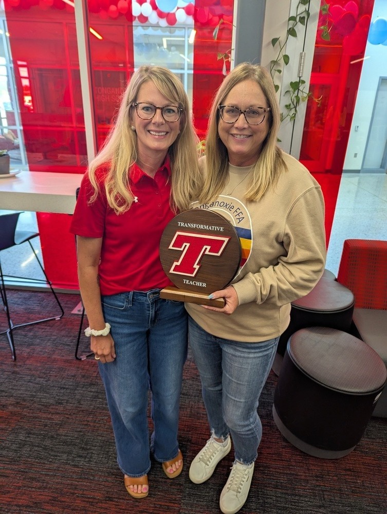 jodie smith wearing a red polo and melanie mcqueen wearing a tan sweatshirt, holding a red tongie t plaque