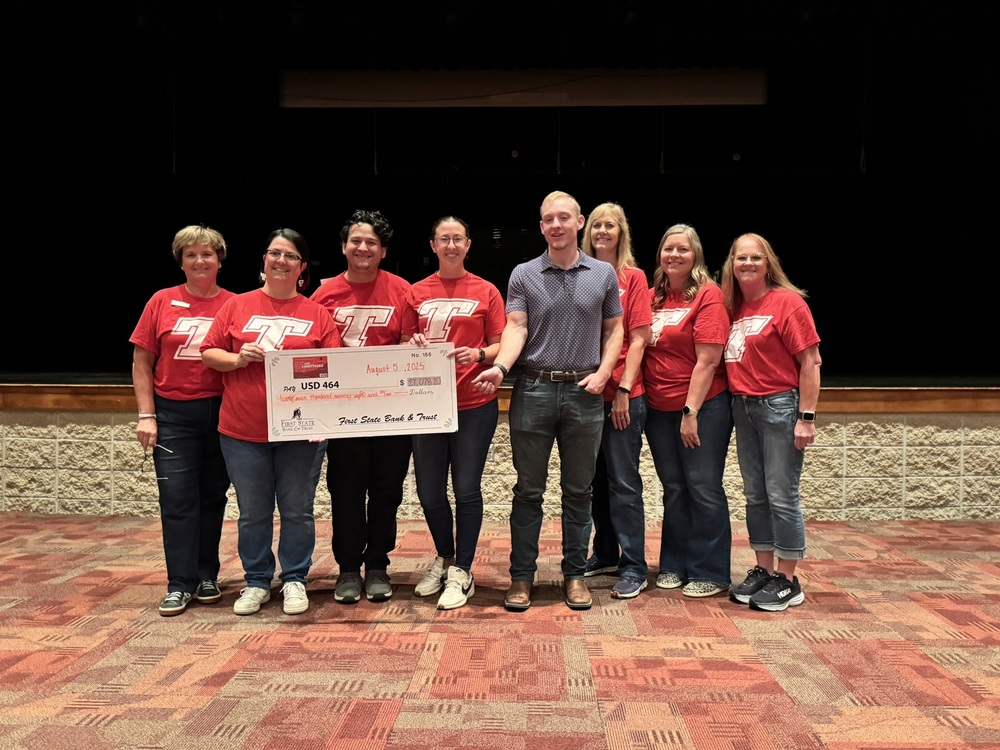 first state bank employees wearing red shirts and jeans hold up a large check