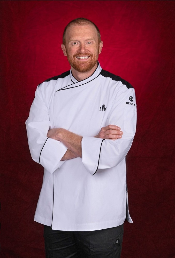 Henry Johnson wearing a white chef's apron and black pants, red backdrop