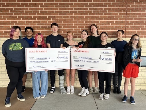 students standing outside in front of a brick wall, holding two large white checks
