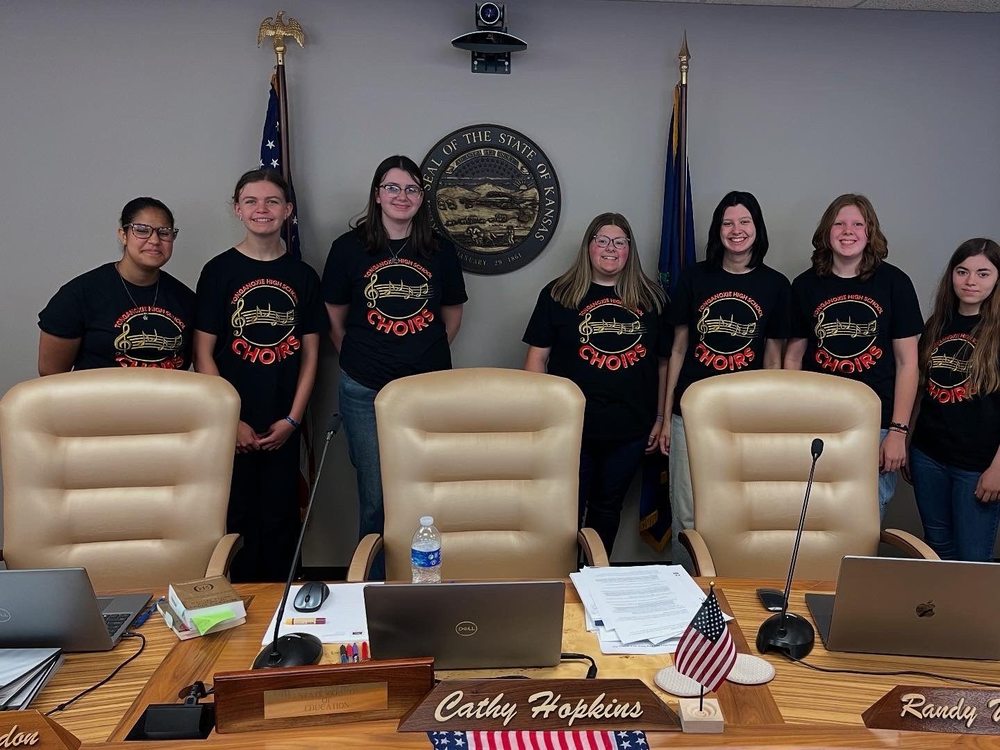 Tongie Choir members wearing matching black shirts stand in front of the seal of Kansas in the State Board of Education Room