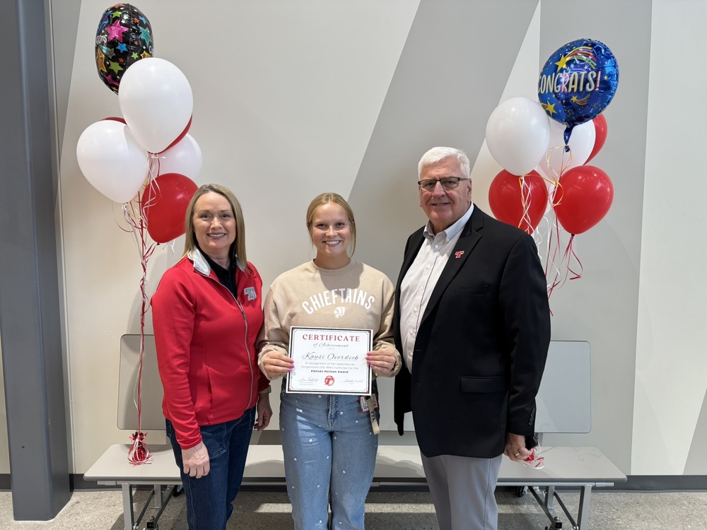 tonya phillips wearing a red shirt and jeans, kaysi overdick wearing a tan sweatshirt and jeans, and loren feldkamp, wearing gray slacks and a black jacket. kaysi holds a paper certificate in her hands