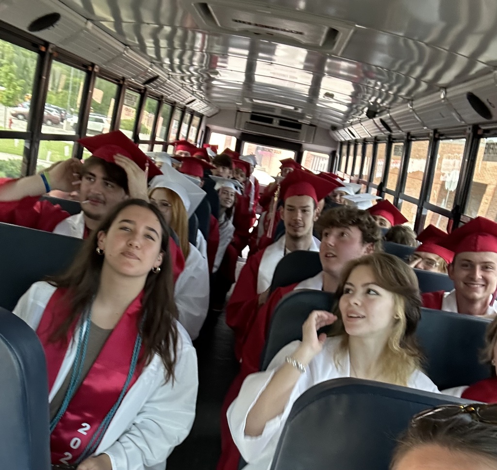 high school seniors wearing caps and gowns sitting on a school bus