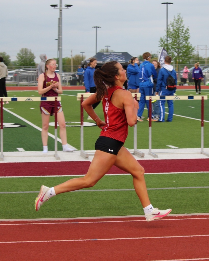 Kara Johnson wearing red tank and black shorts sprinting down the track