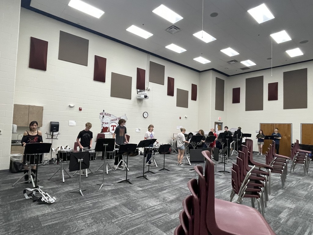 11 drumline members standing in the band room in front of snare drums