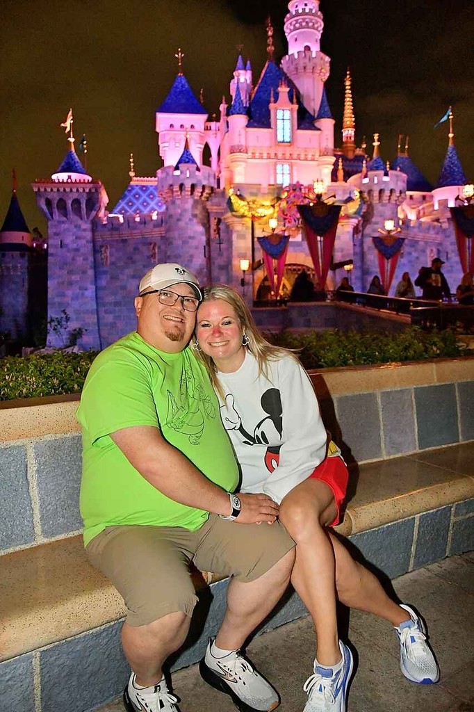 Josh and Amy Olsen sit on a stone bench in front of the Disneyland Castle at night