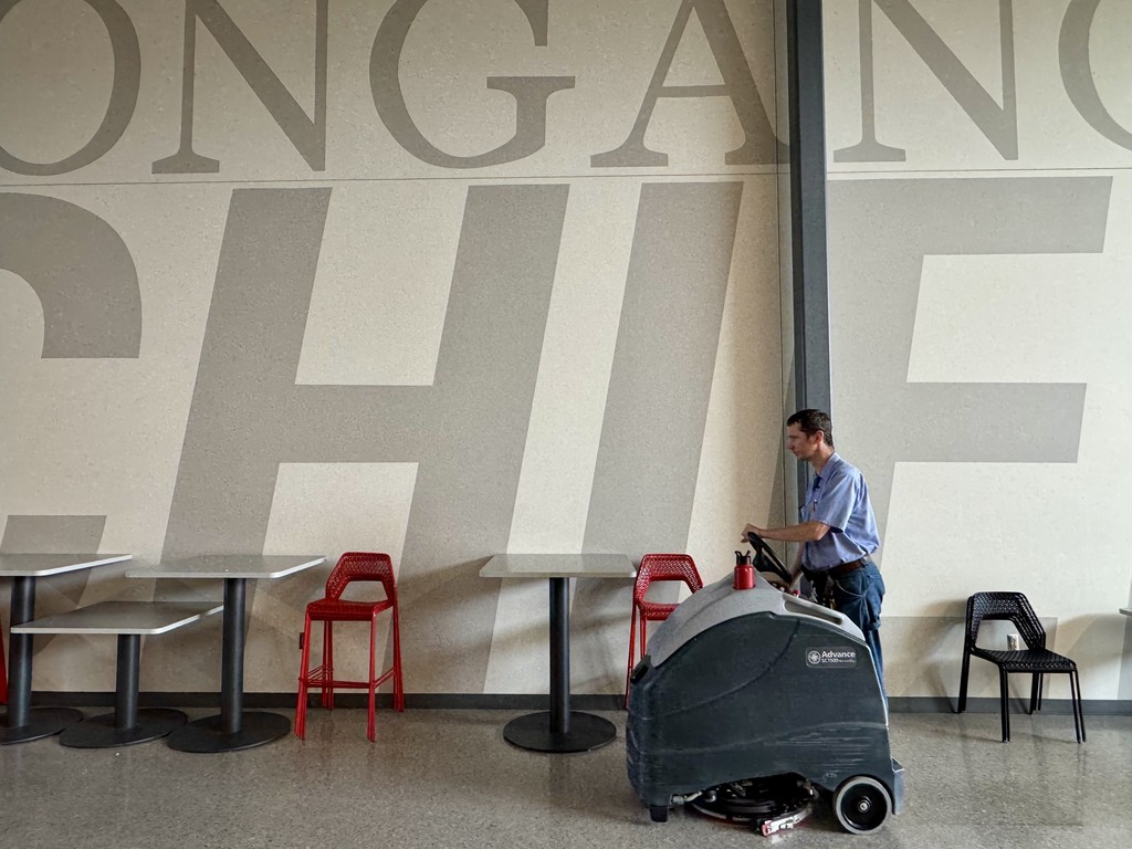 male custodian cleaning the floors on a riding floor scrubber