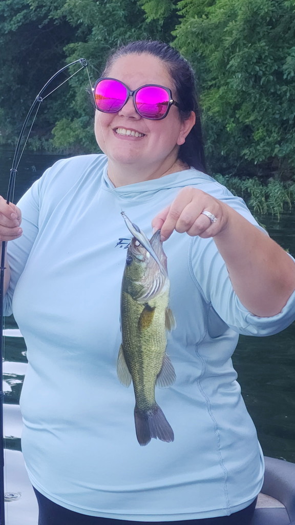 Meagan Vestal wearing purple sunglasses, black pants, and light blue UPF top, holding a hooked fish in her left hand