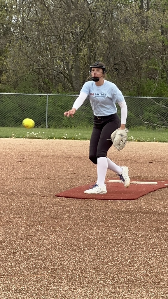 Emma Smith wearing light blue shirt, black softball pants, and cleating, pushing off a pitcher's mound as she release a pitch from the right hand