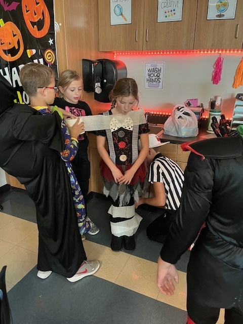 fourth grade students work together to wind toilet paper rolls around a student to create a mummy