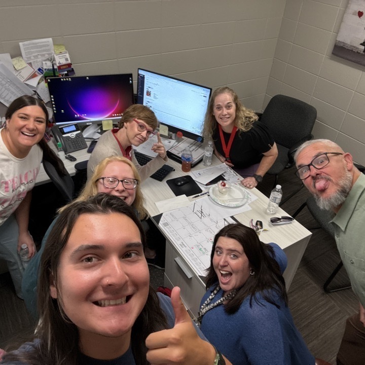 new staff members gather around becky nasalroad at her desk for a selfie