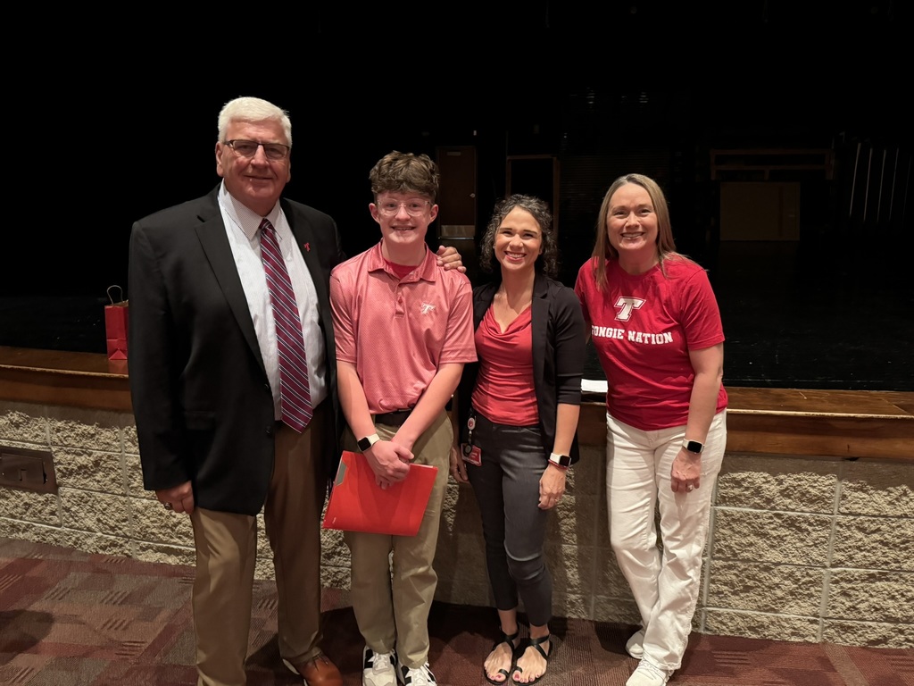 Wesley Emery stands between Loren, Brandy and Tonya. He wears a red polo and khaki pants and holds a red folder