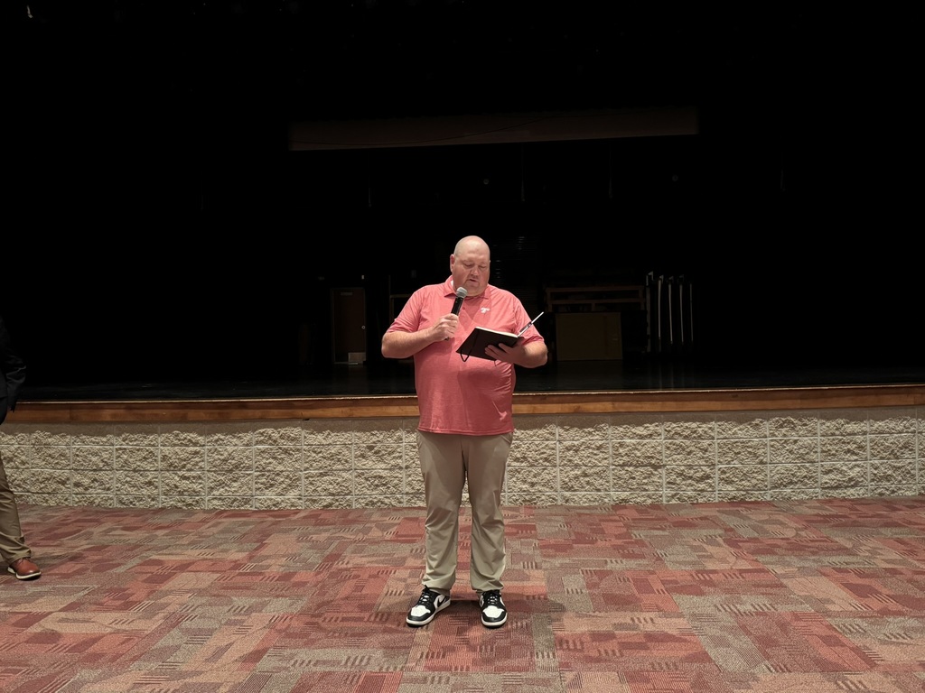 board president Justin Sturgeon, wearing a red polo and khakis, holding a microphone and a notebook