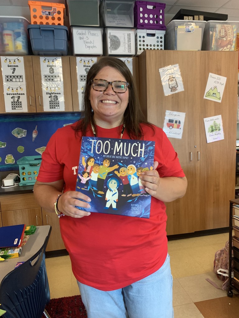 1st grade teacher in red shirt holding a book called "Too Much" 