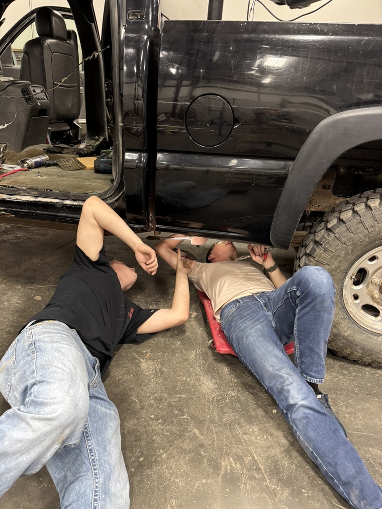 two students on their back, looking up under a truck