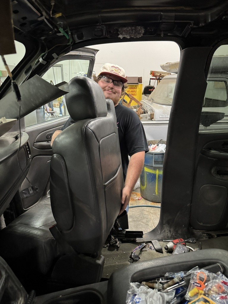 male student wearing black t shirt and white hat, pulling a leather chair out of a truck bed