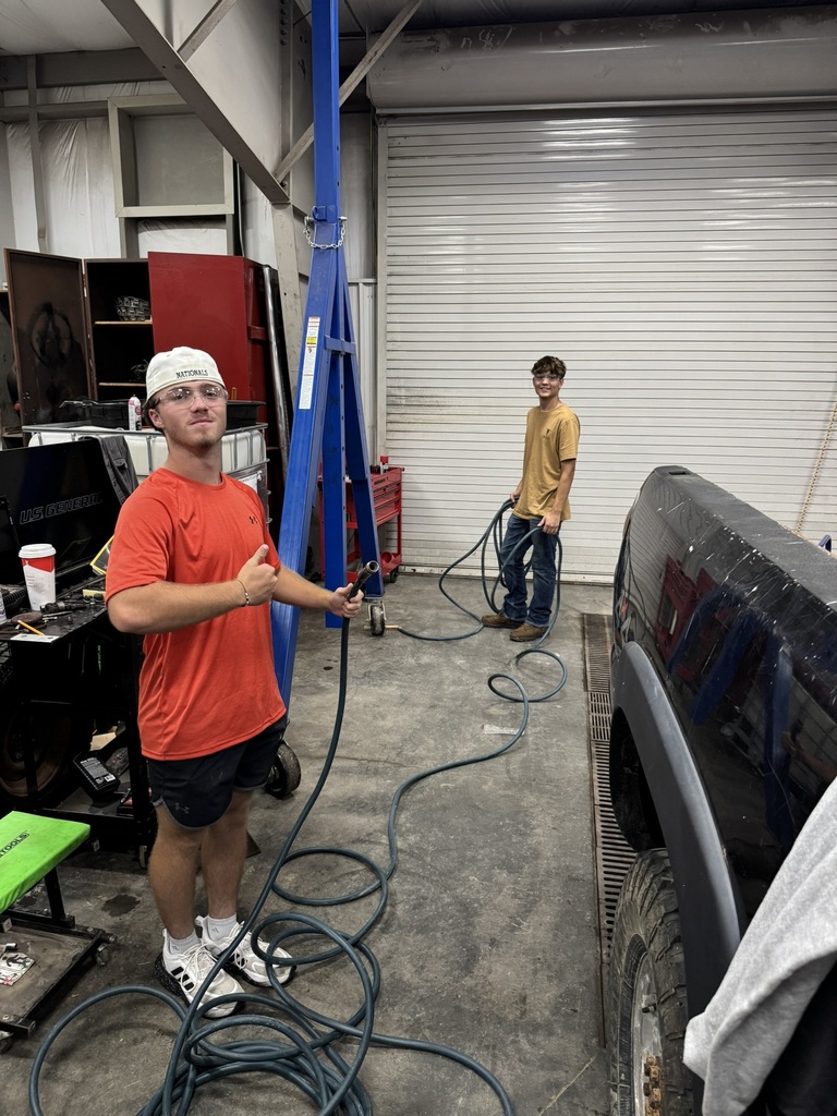 two male students running hoses to a black pickup truck