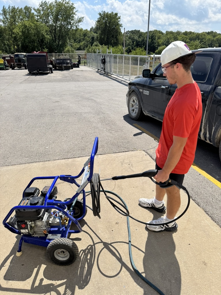 male student wearing red shirt and black shorts, working on a power washer
