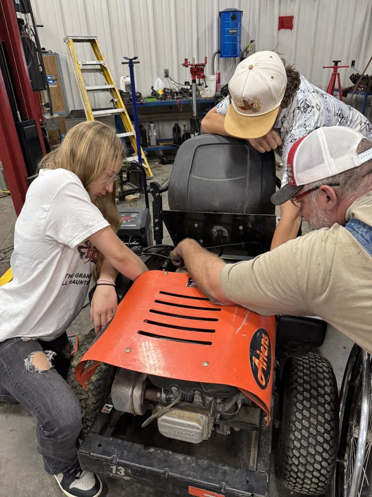 two student and Mr. Maurer diagnose a lawn mower repair