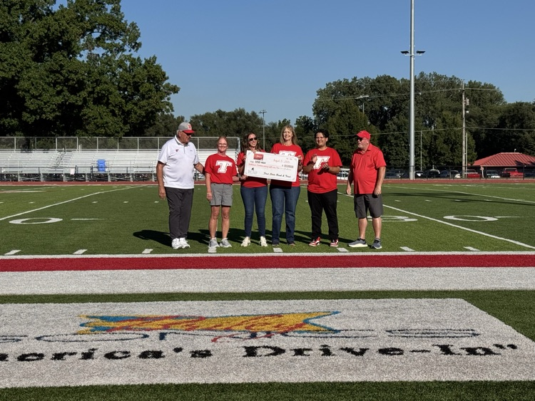 Bank employees and superintendent wearing red shirts standing on the football field, accepting a check