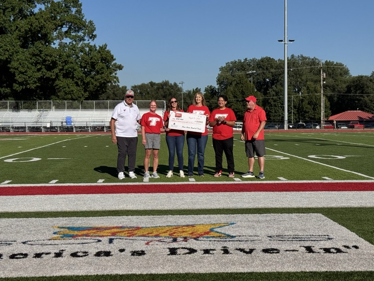 Bank employees and superintendent wearing red shirts standing on the football field, accepting a check