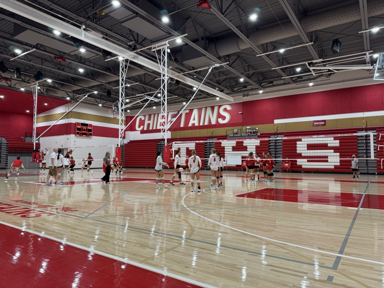 High school girls wearing red or white jerseys playing volleyball in a high school gymnasium