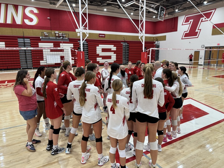 High school girls wearing red or white jerseys playing volleyball in a high school gymnasium