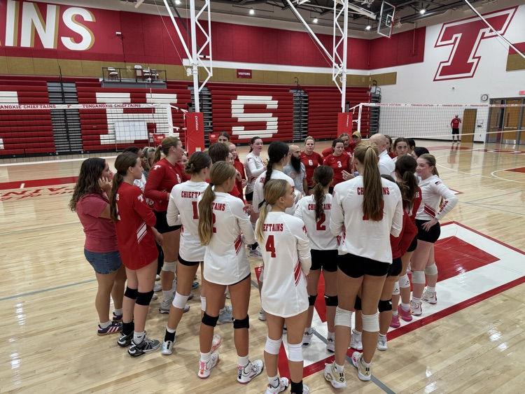 High school girls wearing red or white jerseys playing volleyball in a high school gymnasium