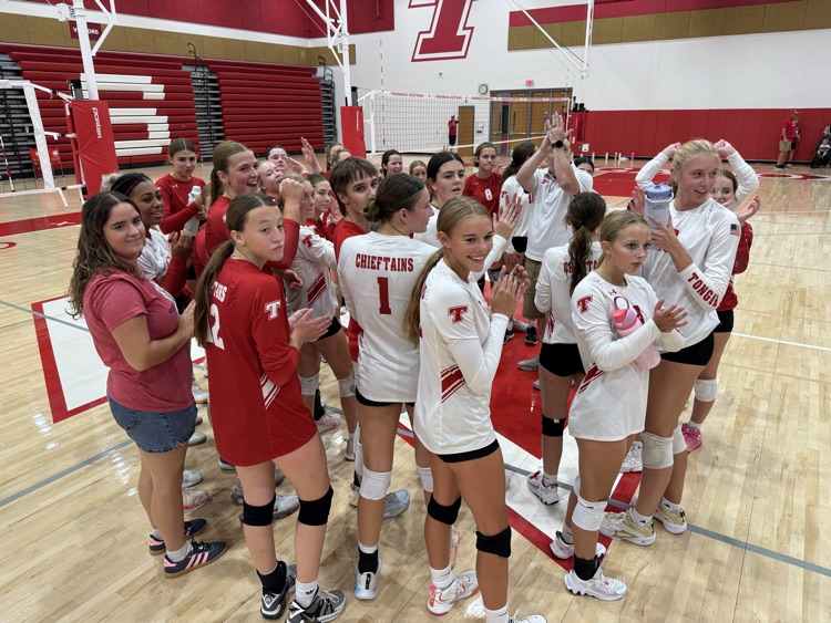 High school girls wearing red or white jerseys playing volleyball in a high school gymnasium