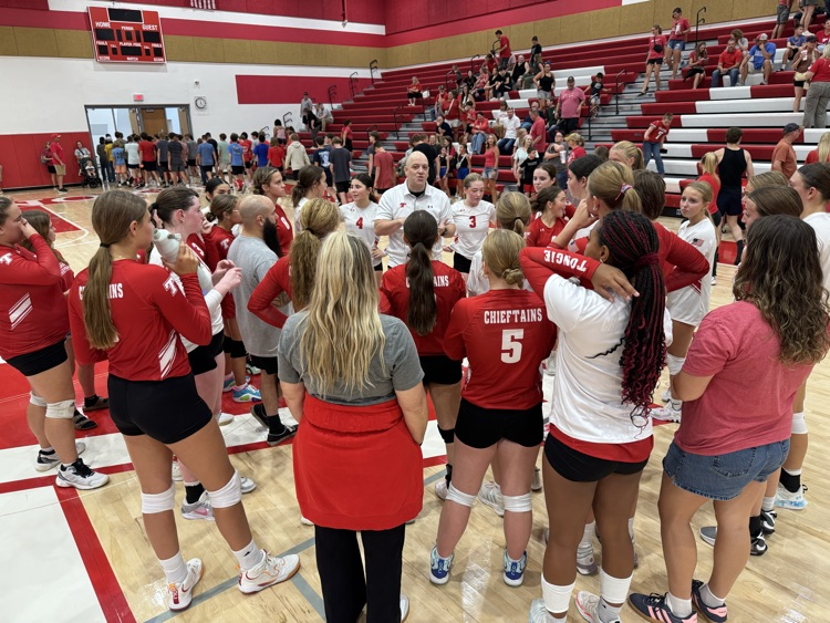High school girls wearing red or white jerseys playing volleyball in a high school gymnasium