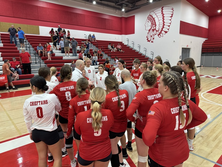 High school girls wearing red or white jerseys playing volleyball in a high school gymnasium
