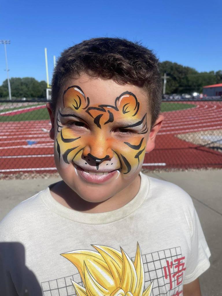 a boy wearing a gray t shirt with his face painted like a tiger