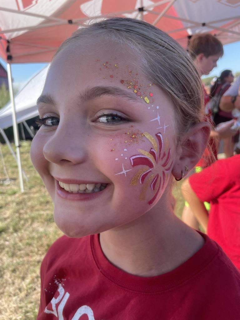 girl with a red and gold firework and glitter painted on the left side of her face